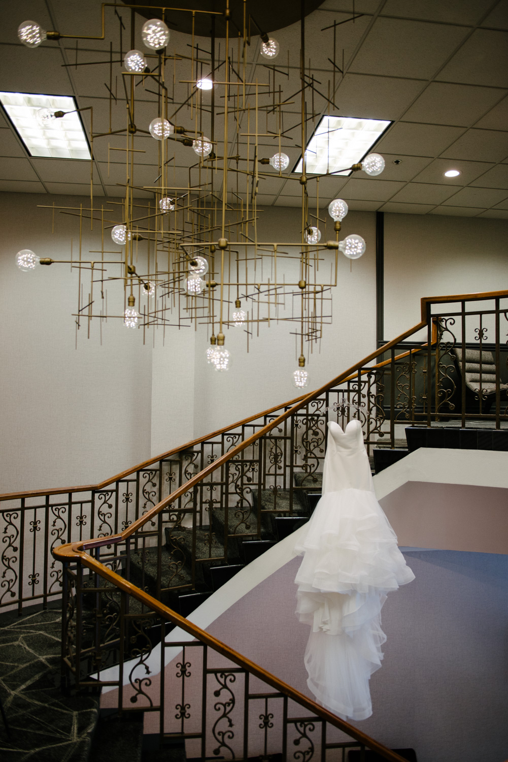 Wedding Dress hanging on stair case under chandelier at the Concourse Hotel in Madison, WI