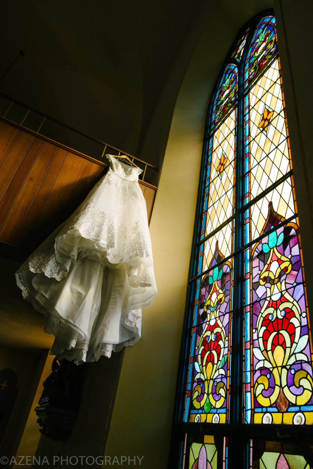 wedding dress hanging in front of stain glass windows
