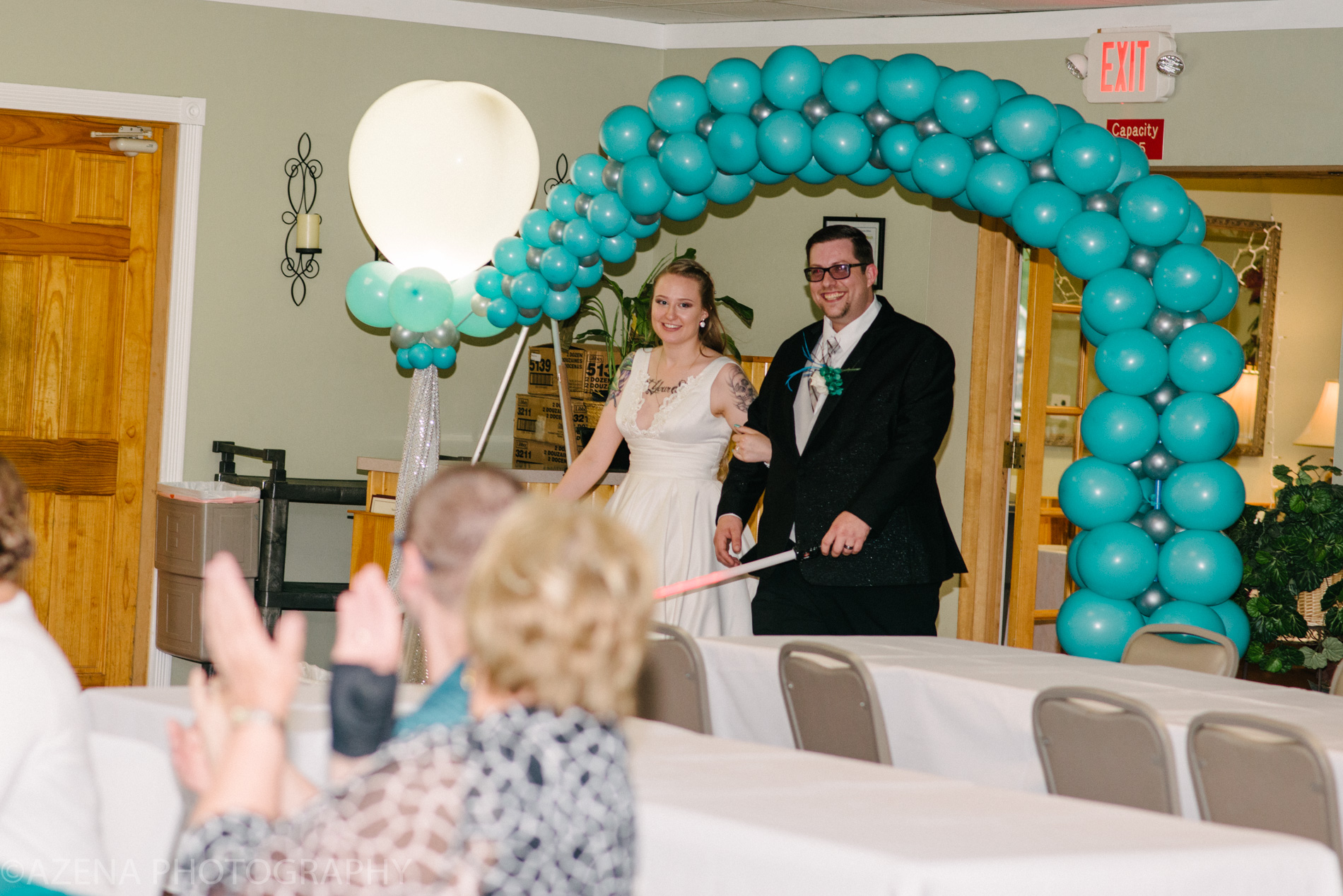 bride and groom walking under teal balloon display